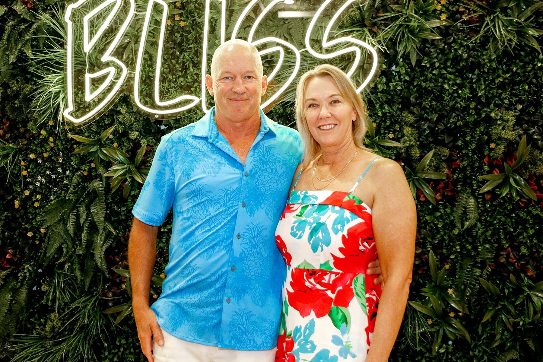 Man and woman in front of a green wall with neon 