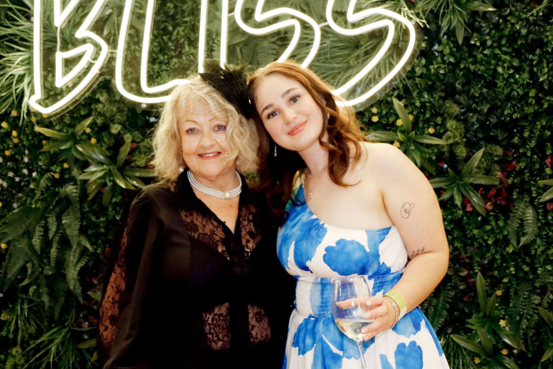 Two women smiling, posing in front of a neon 