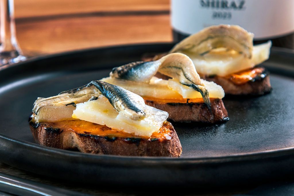 Toasted bread slices topped with fish, cheese, and vegetables on a black plate.