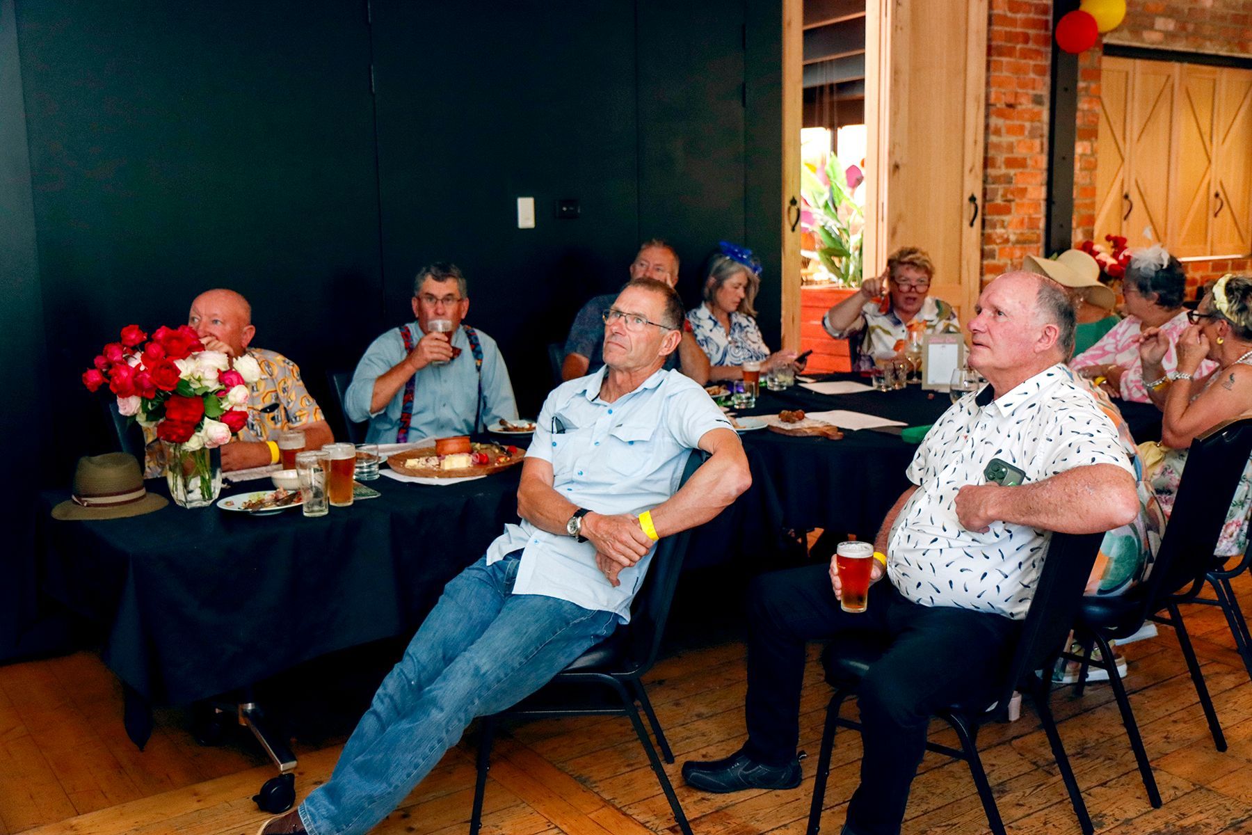 A group of people at a table, some looking at something off-screen, possibly a party.
