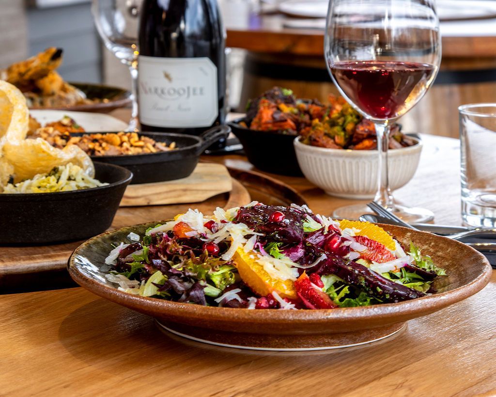 Salad with oranges, beets, and black beans, with wine and various dishes on a wooden table.