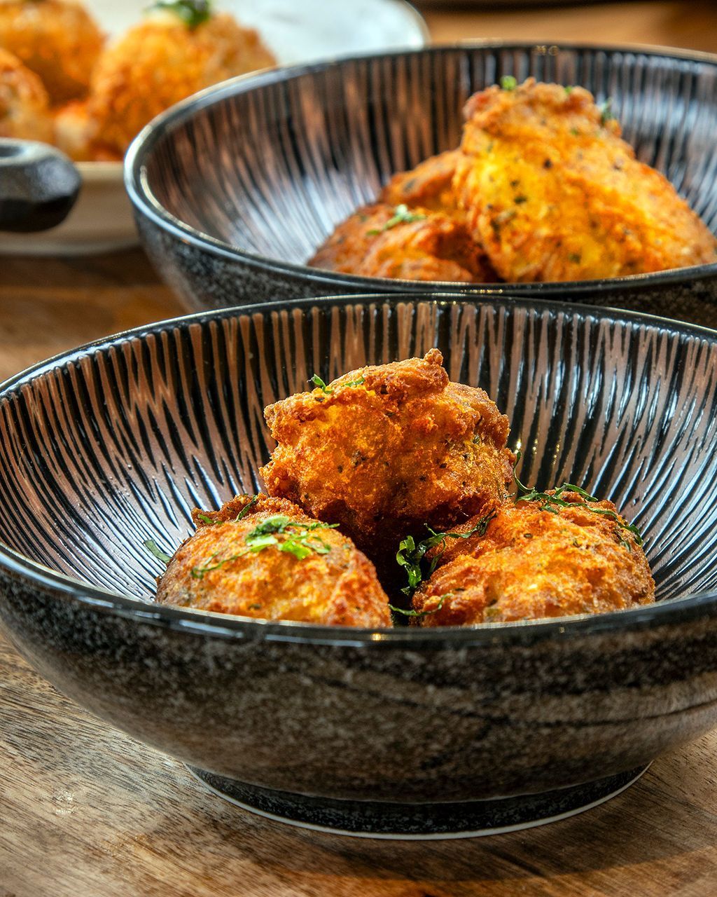 Three bowls of fried food, likely appetizers, with textured black and white bowls on a wooden table.