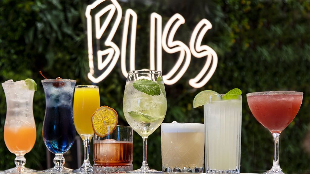 Various cocktails on a bar, under a neon
