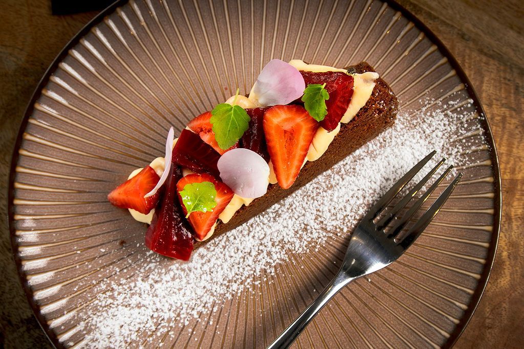 Dessert on a brown plate: rectangular cake, cream, strawberries, mint, and sugar dusting.