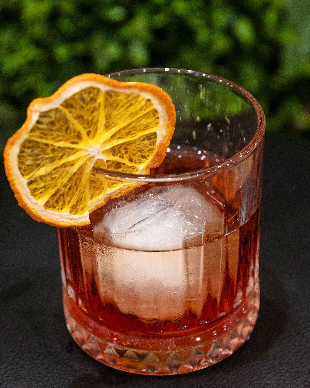 Cocktail in a short, patterned glass with orange slice garnish and ice.