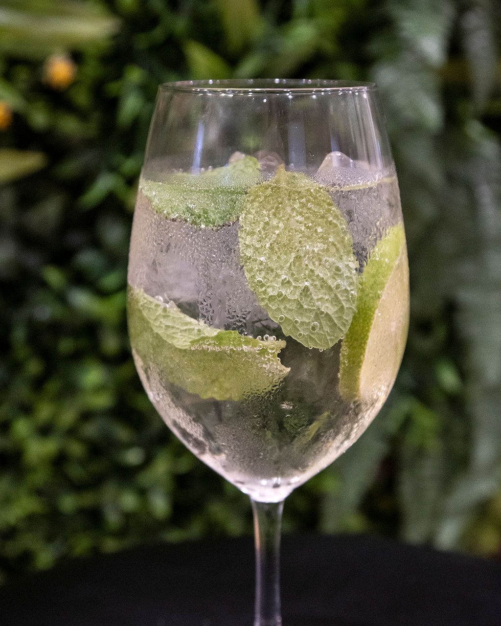 Cocktail in a tall glass with mint leaves and lime, on a black surface with a green background.