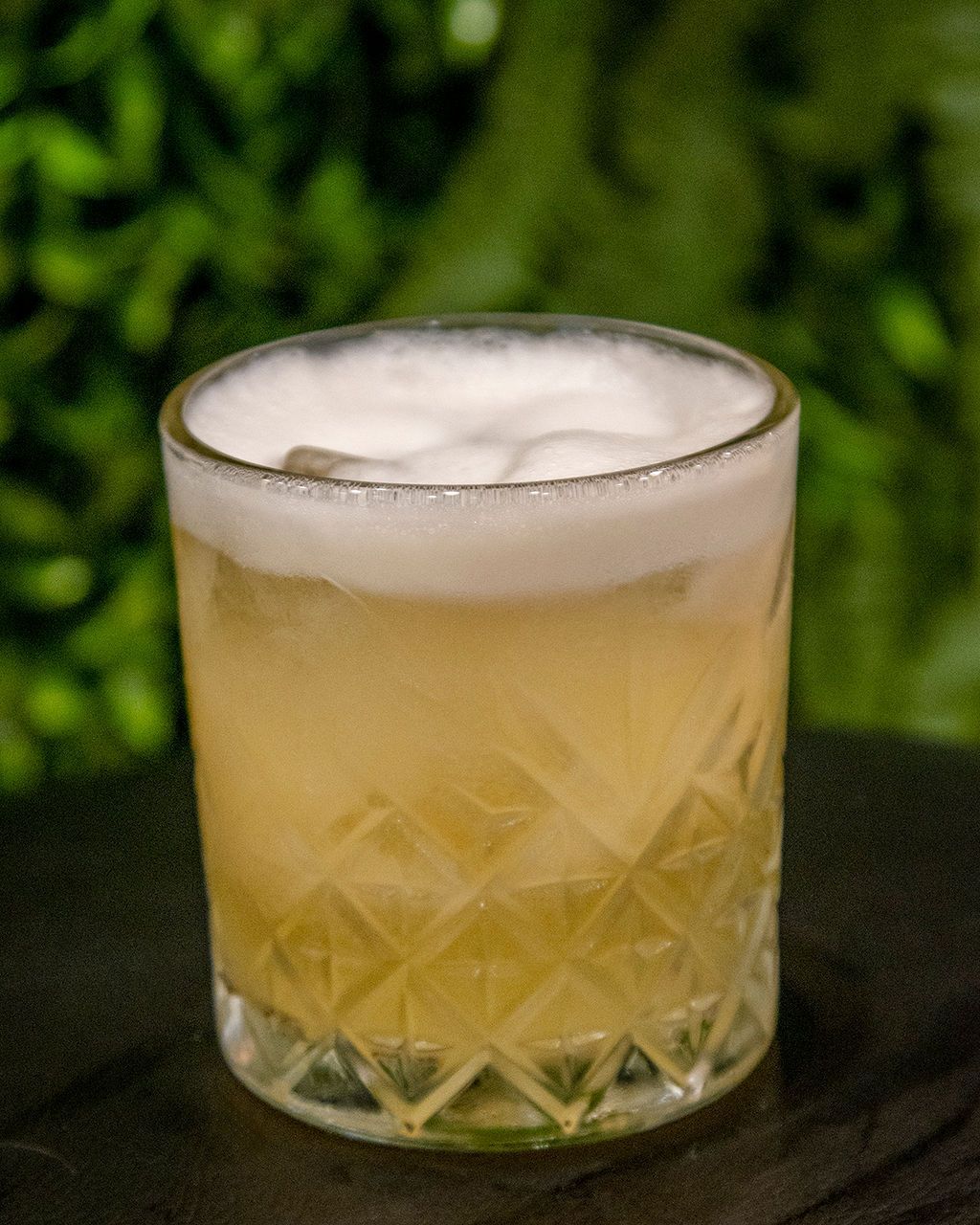 Cocktail in a diamond-cut glass with a foamy top, set against a green, blurry background.