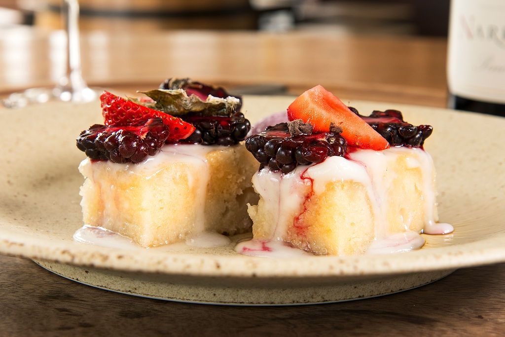 Dessert: White cake squares topped with berries and drizzled with cream on a tan plate.
