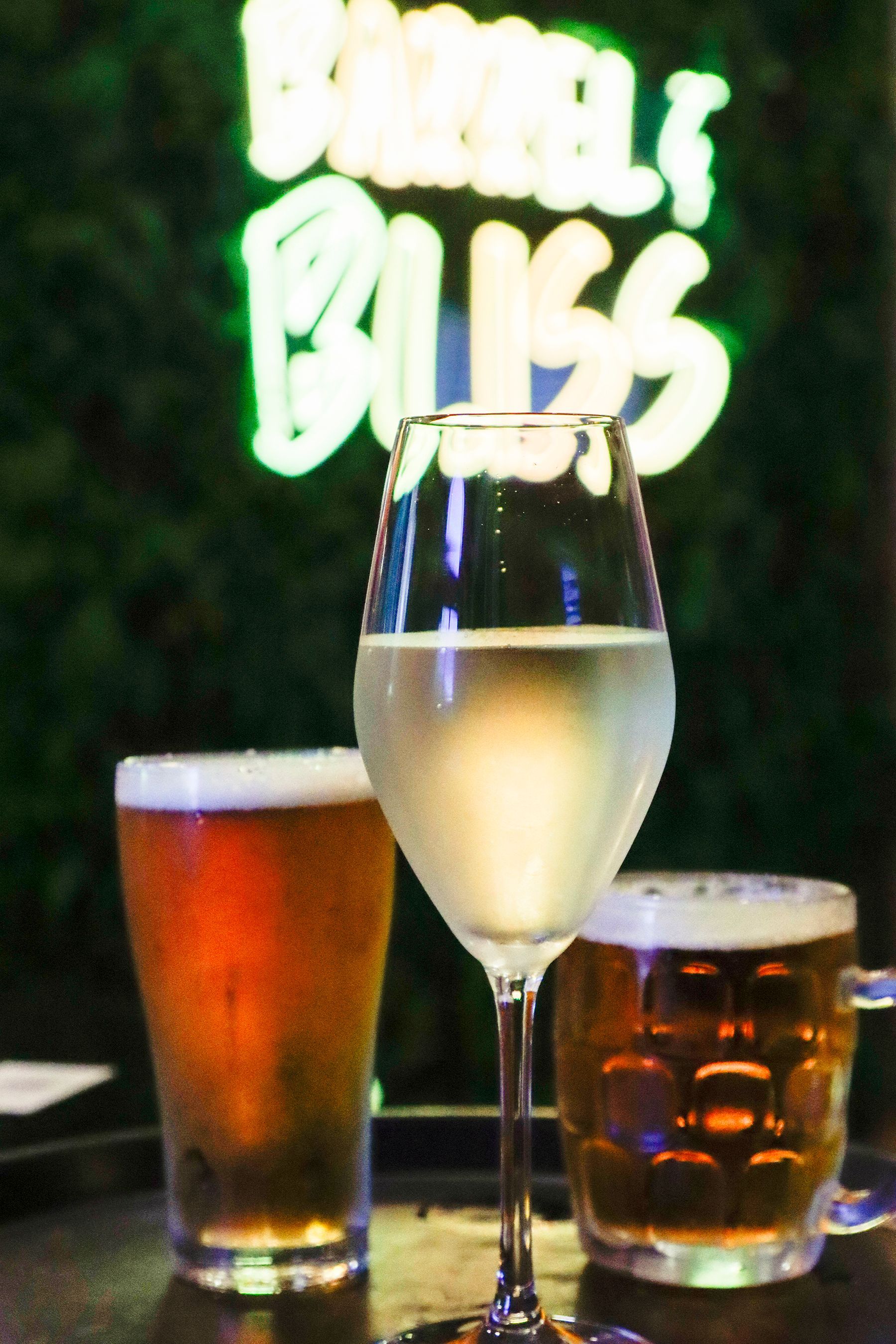 Three drinks: beer in a pint glass and mug, white wine in a glass, with a neon 
