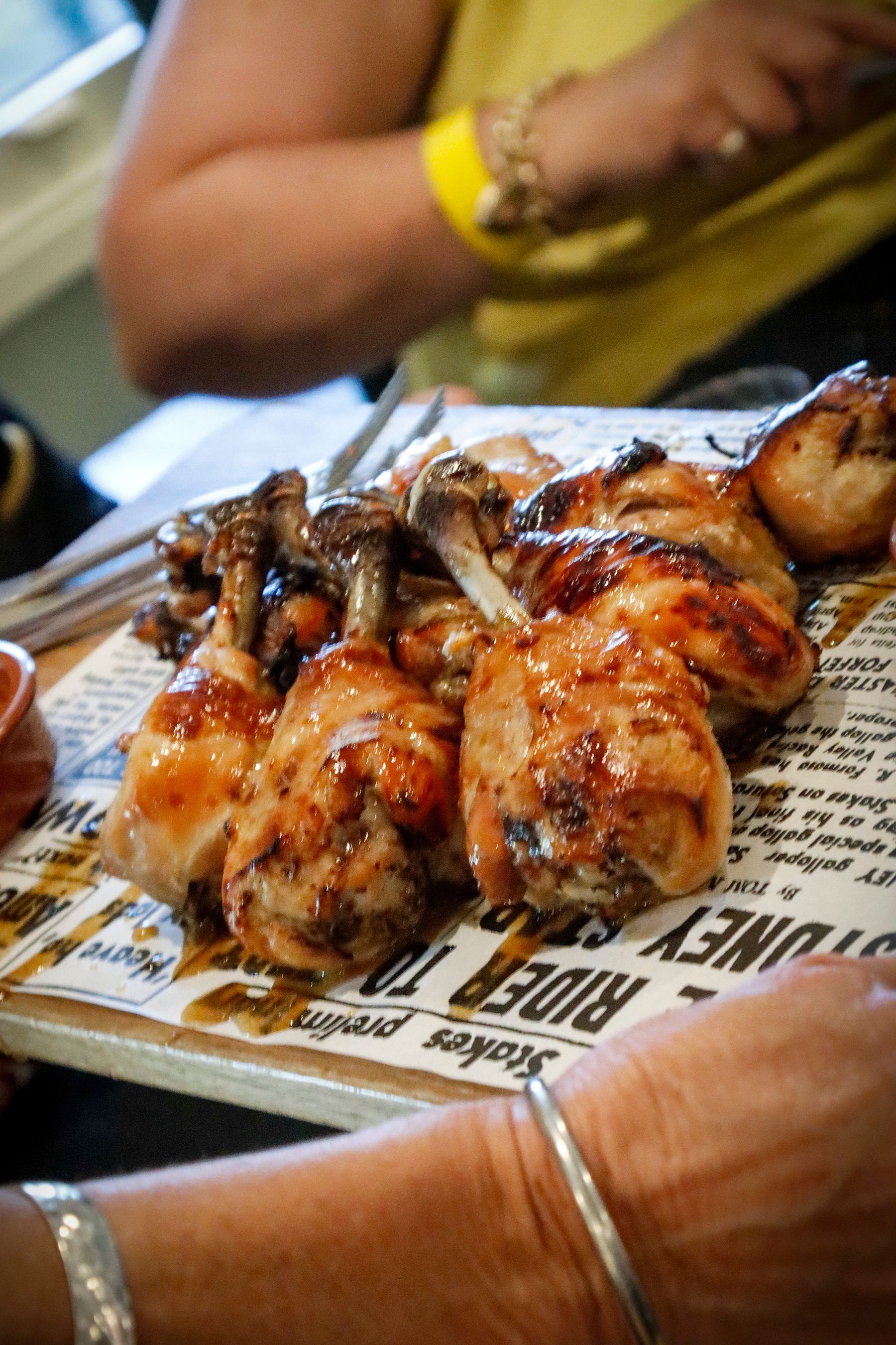 Grilled chicken drumsticks on newsprint, served on a wooden board at a table.