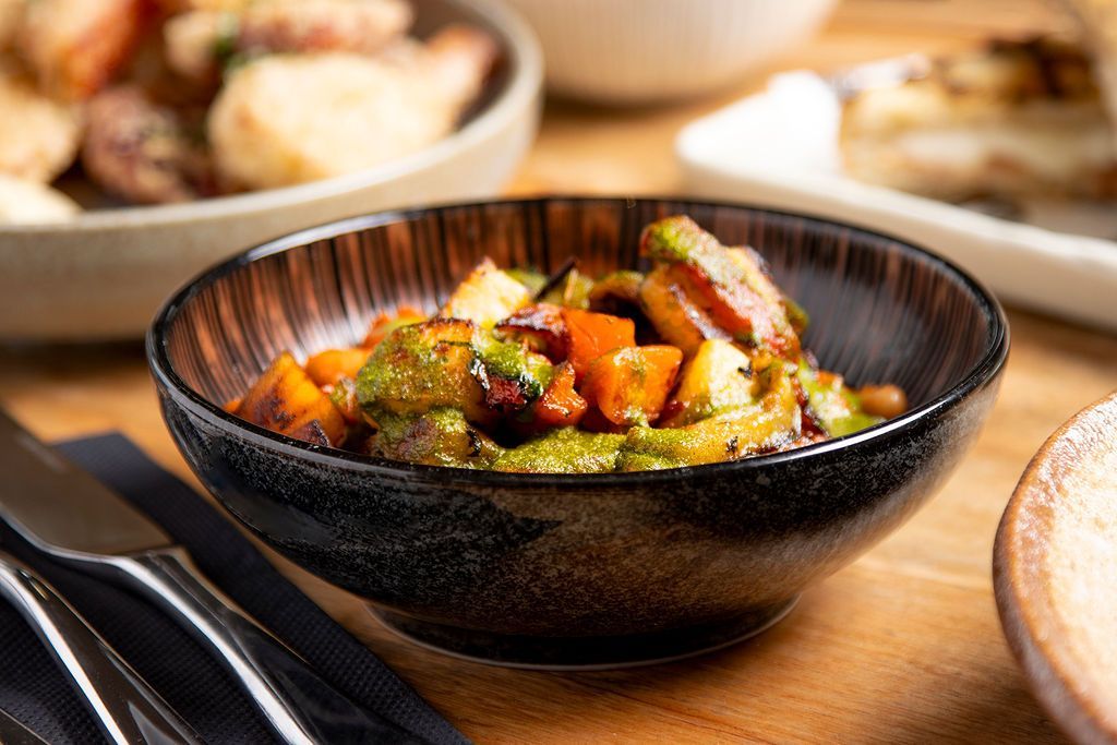 Bowl of colorful roasted vegetables, with a table setting.