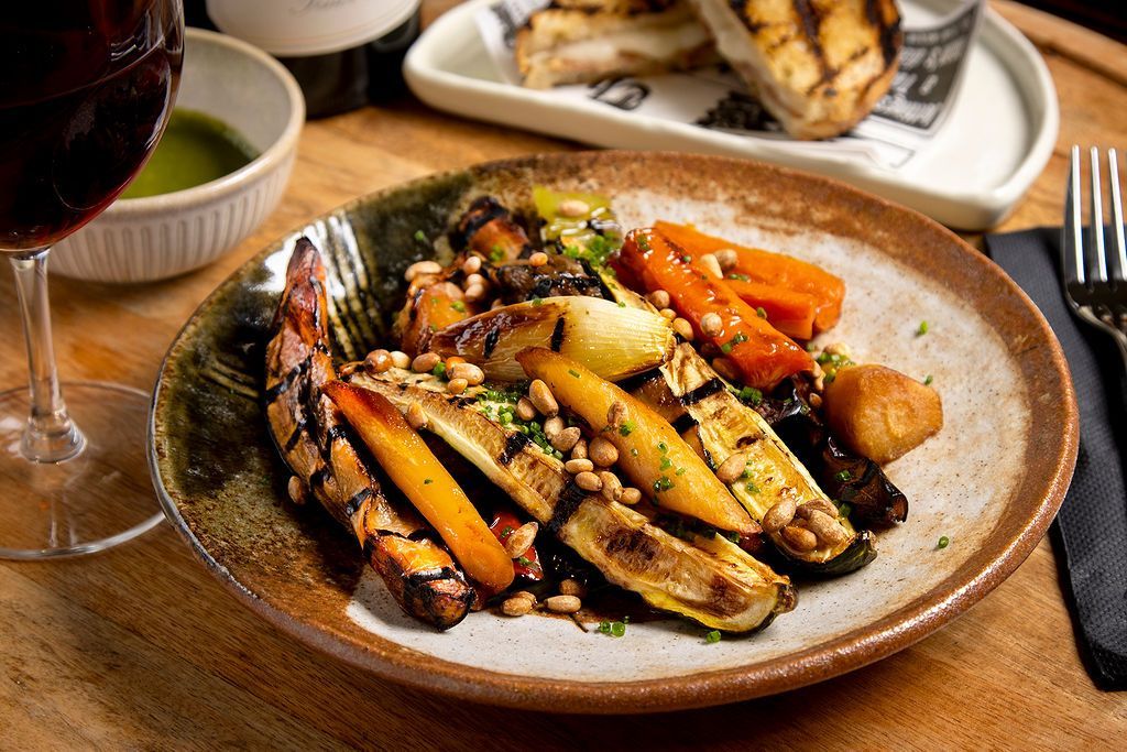 Grilled vegetables with pine nuts on a plate, a glass of red wine, and grilled sandwiches.