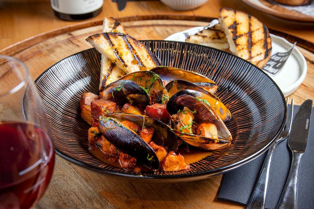 Mussels in tomato sauce with grilled bread and red wine on a wooden table.