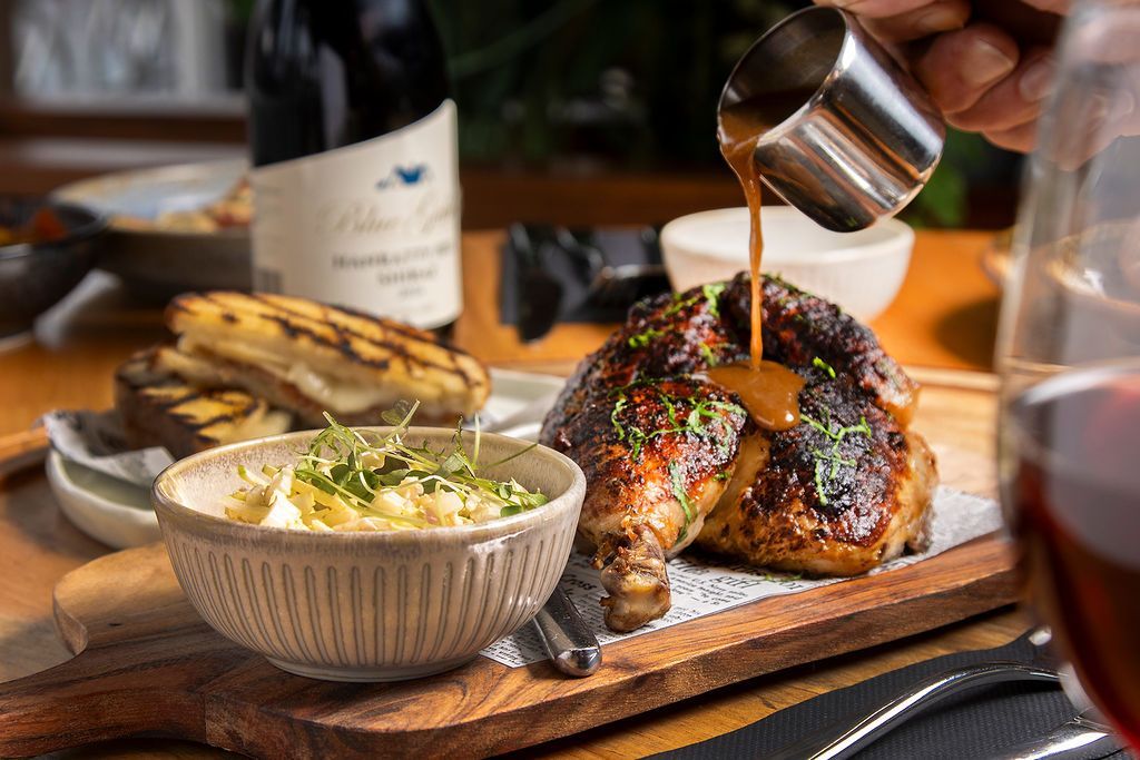 Roasted chicken with gravy, mashed potatoes, and grilled bread on a wooden board, with wine.