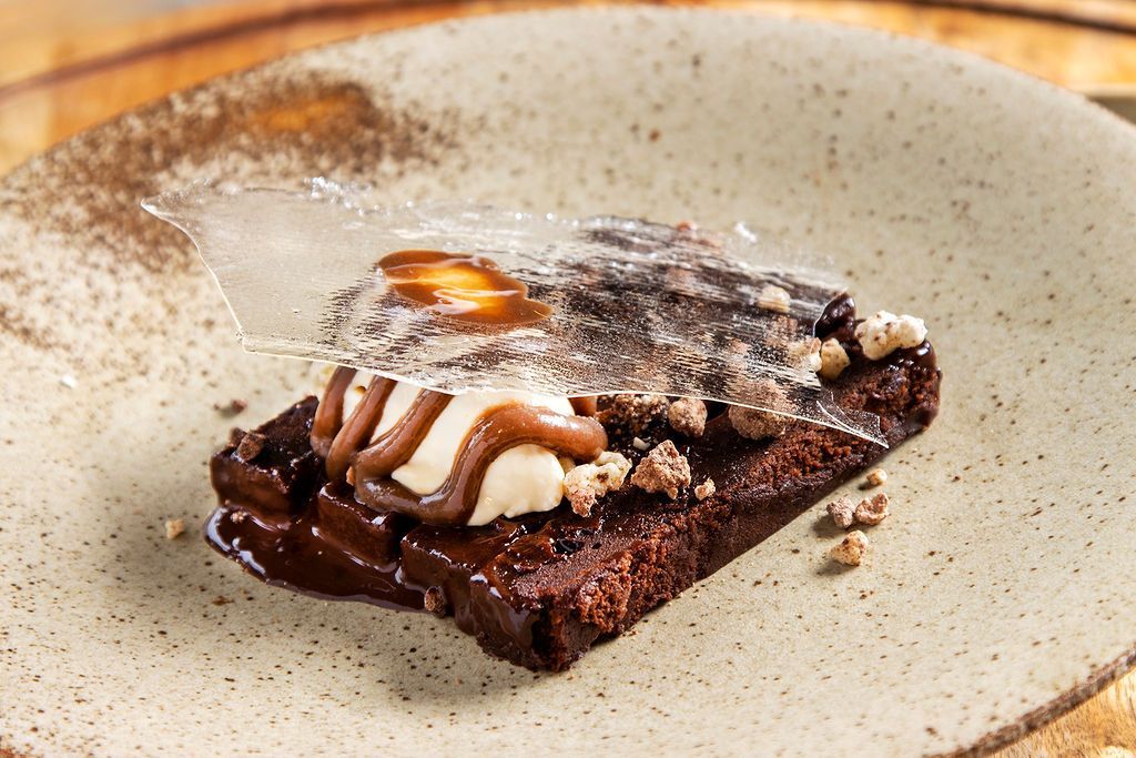 Brownie dessert with cream, caramel, and sugar crystal on a plate.
