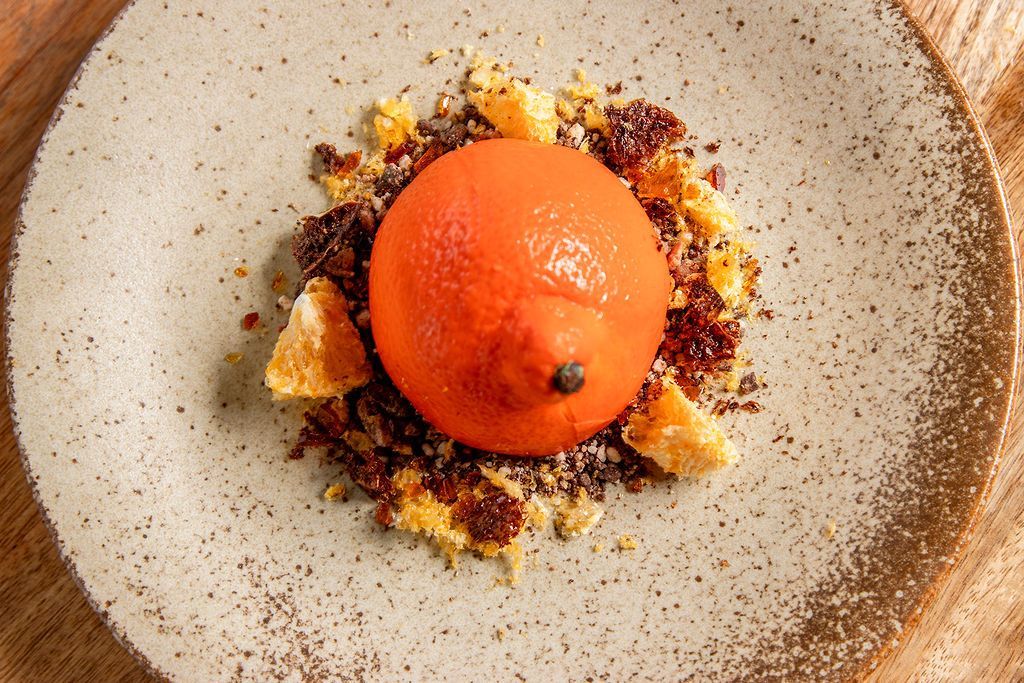 Orange dessert with crumbled biscuit and chocolate on a speckled plate.