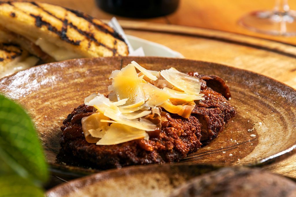 Plate of food: dark meat topped with cheese, with grilled plantains in the background.
