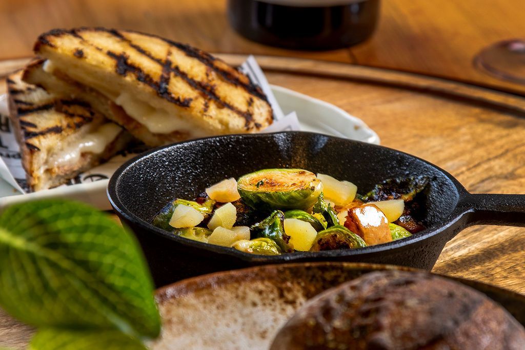 Grilled cheese sandwich with brussels sprouts in a skillet, on a wooden table.