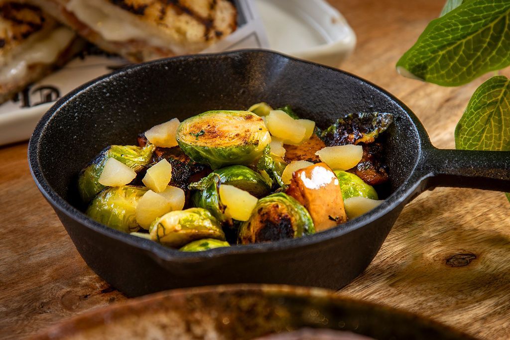 Roasted Brussels sprouts in a black cast iron skillet, with diced pineapple and dark bits, on a wooden surface.
