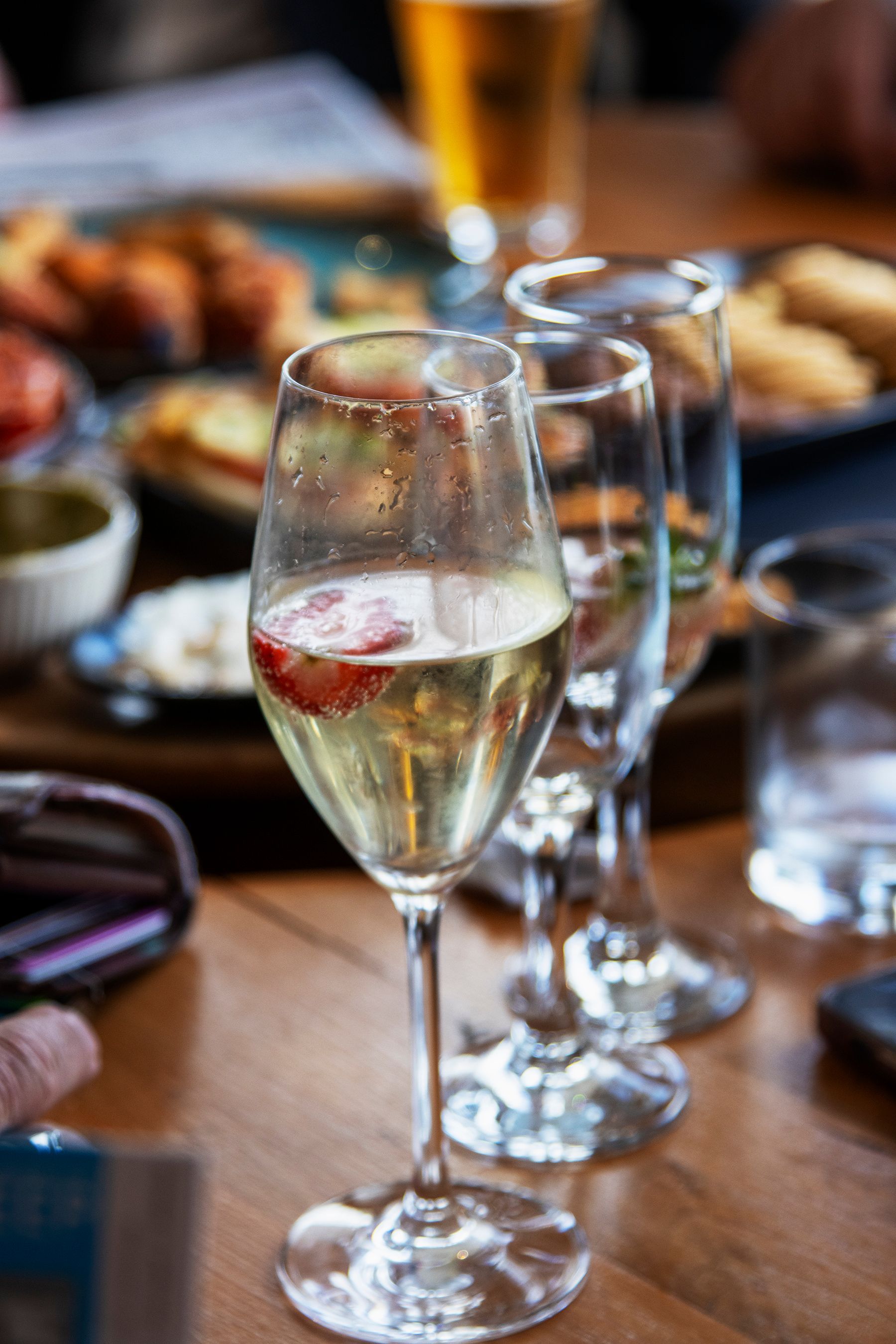Champagne glass with strawberry slice, other glasses, food, wooden table.