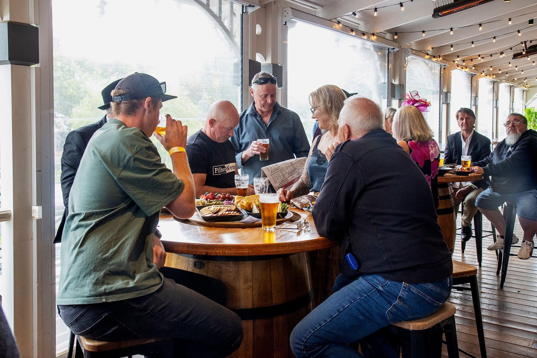 People gathered around a barrel table in a bar, enjoying drinks and snacks.
