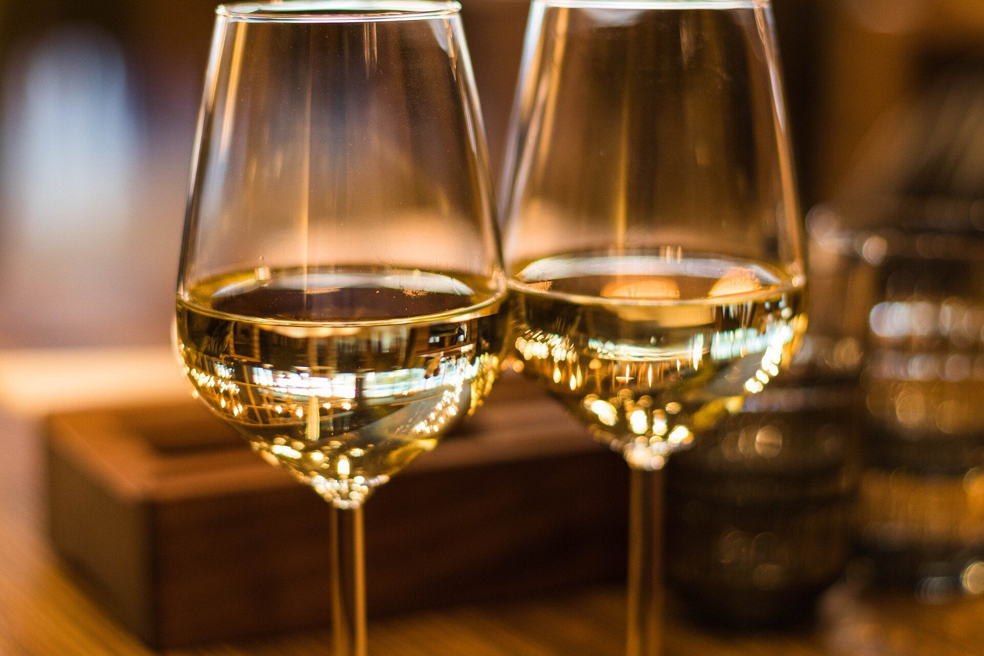 Two glasses of white wine on a wooden table, reflecting the room, a blurred background.