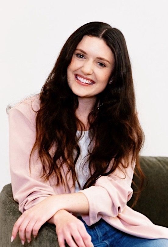 A woman is sitting on a couch with her legs crossed and smiling.