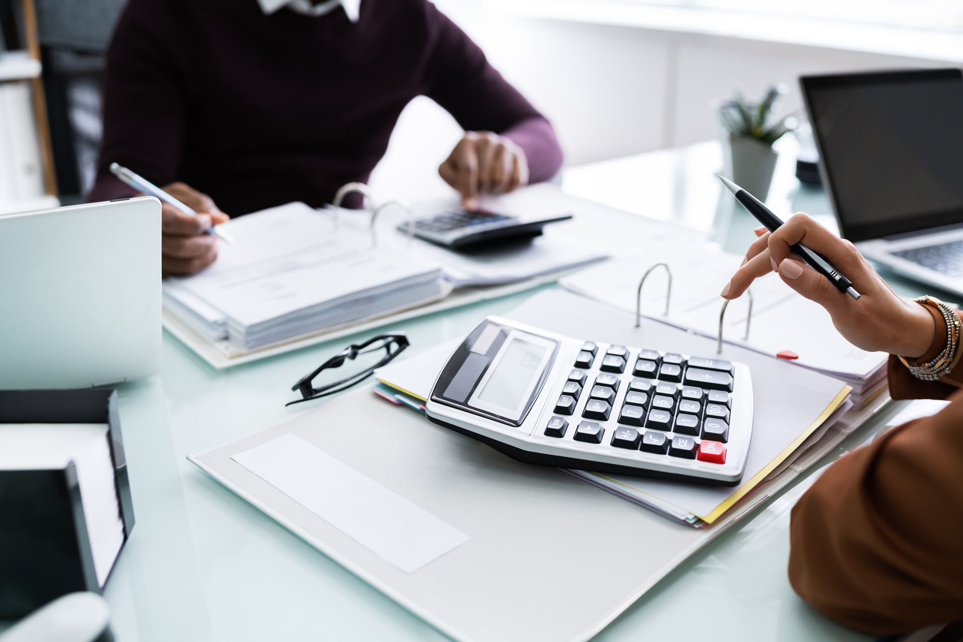 Two people are sitting at a table with a calculator and a laptop.