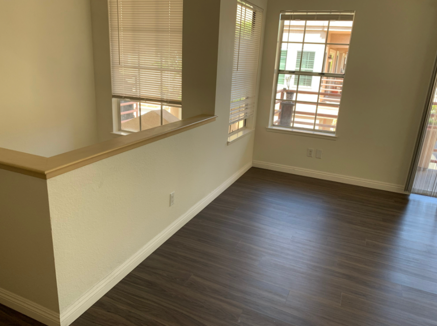 an empty living room with hardwood floors and two windows .