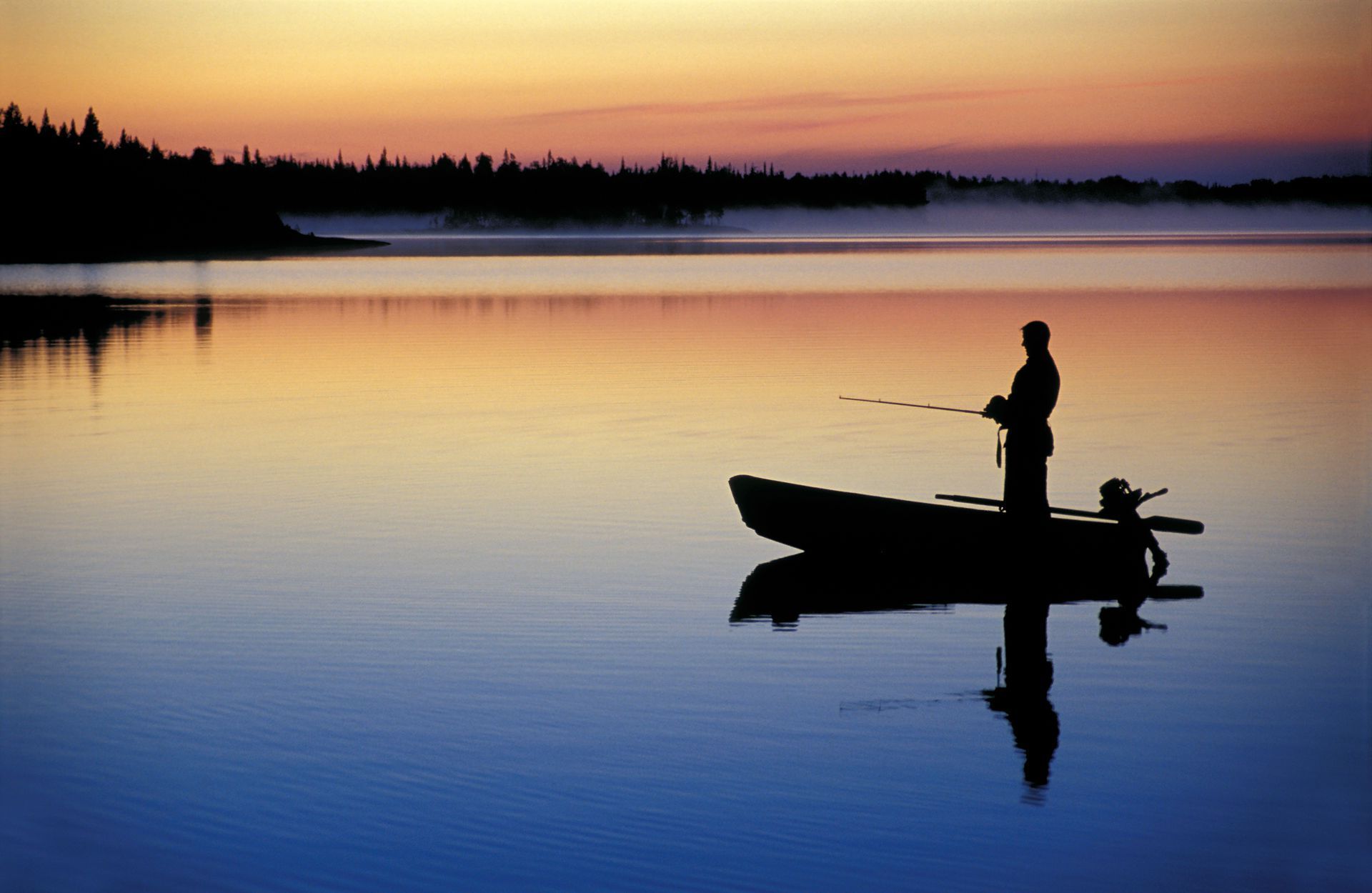 a man is fishing in a boat on a lake at sunset