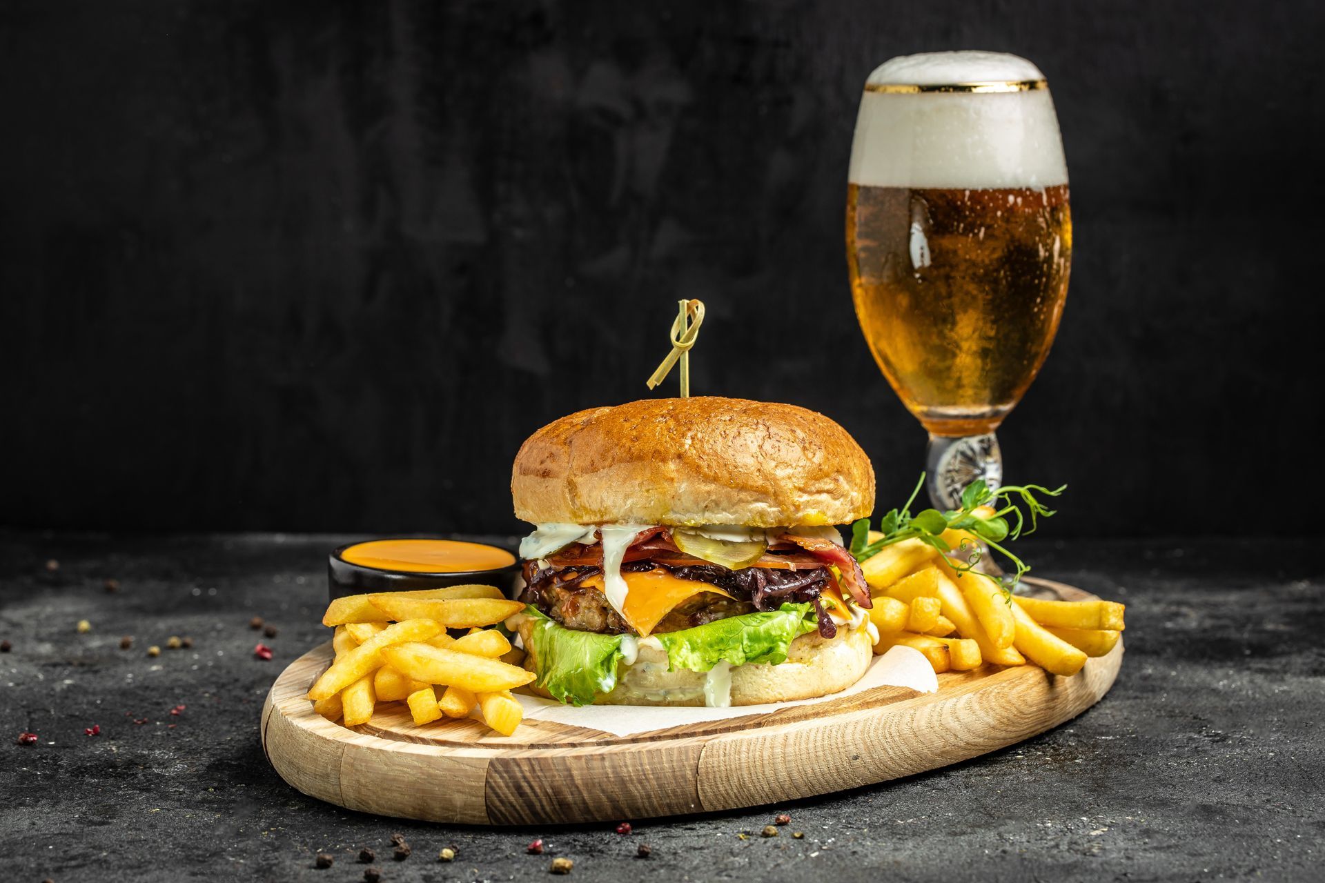 a hamburger and french fries on a wooden cutting board next to a glass of beer .