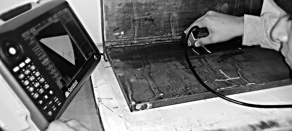A person uses an ultrasonic testing device to inspect a metal weld on a dark surface.
