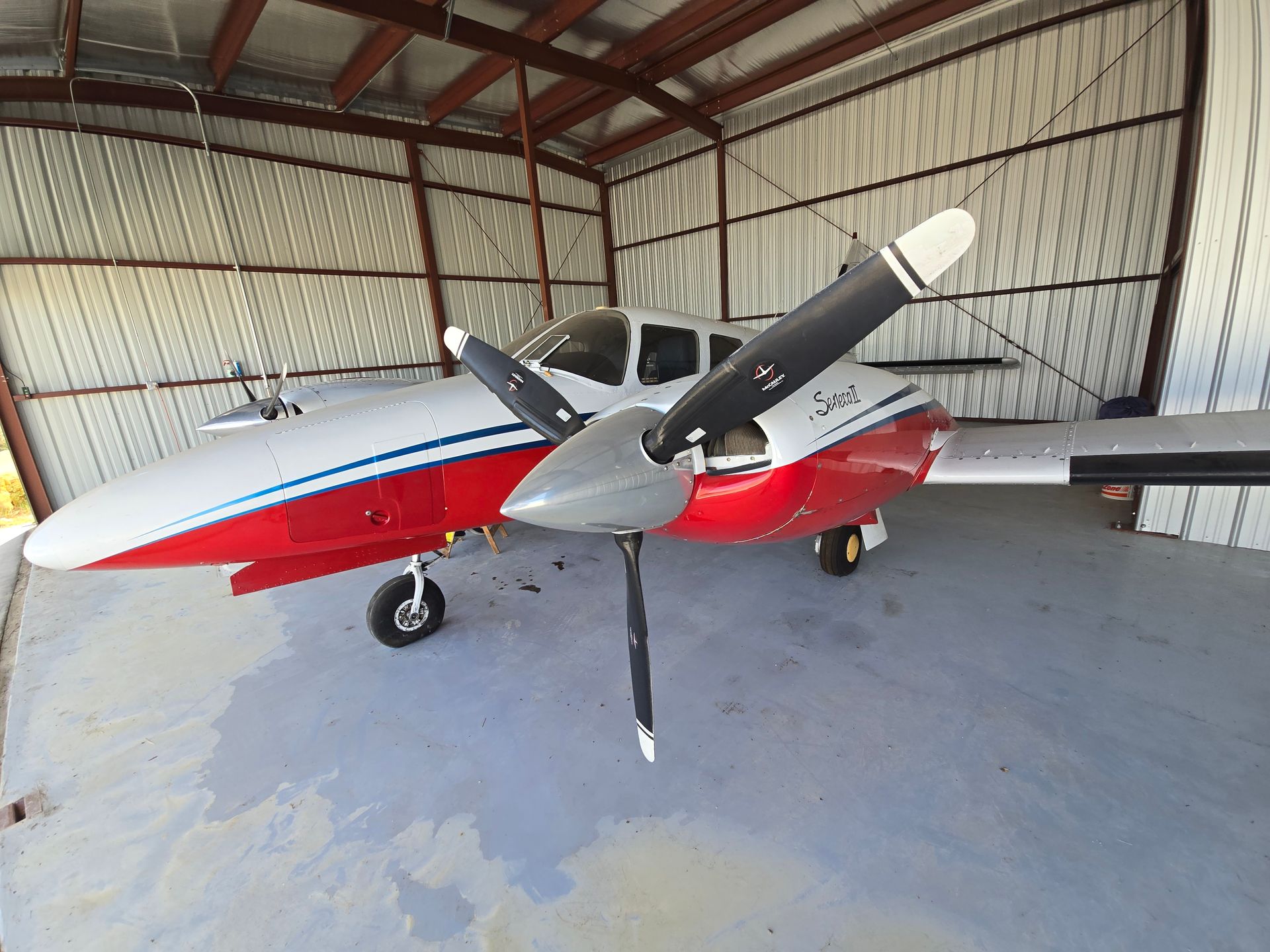 A red and white twin-engine propeller aircraft parked inside a metal hangar.