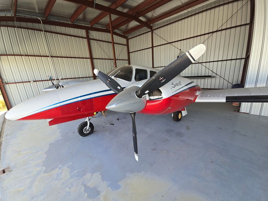 A red and white twin-engine propeller aircraft parked inside a metal hangar.