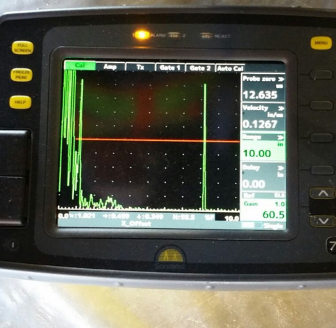 Ultrasonic flaw detector screen displaying a green signal wave against a black background with numerical data readouts.