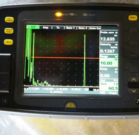 Ultrasonic flaw detector screen displaying a green signal wave against a black background with numerical data readouts.