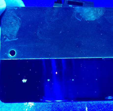 A dark metal surface with a circular hole on the left, illuminated by blue light with small, bright reflections below.