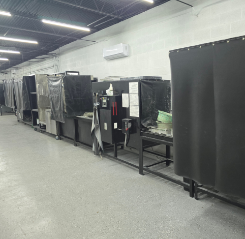 A row of black metal workstations with privacy curtains in a warehouse space with light gray floors and white walls.