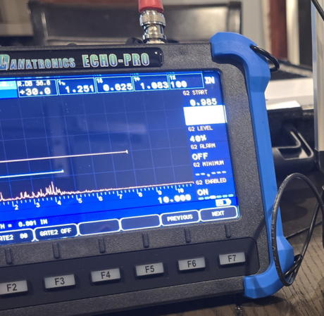 A Danatronics Echo-Pro ultrasonic thickness gauge displaying digital measurements and a signal waveform on its screen.