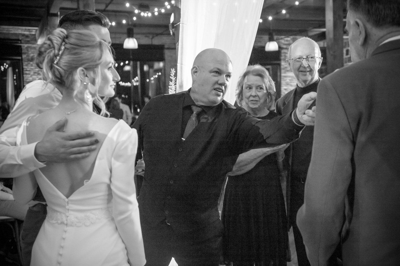 DJ Aaron Bracken holds the microphone at an Indianapolis wedding reception surrounded by the bride and groom.