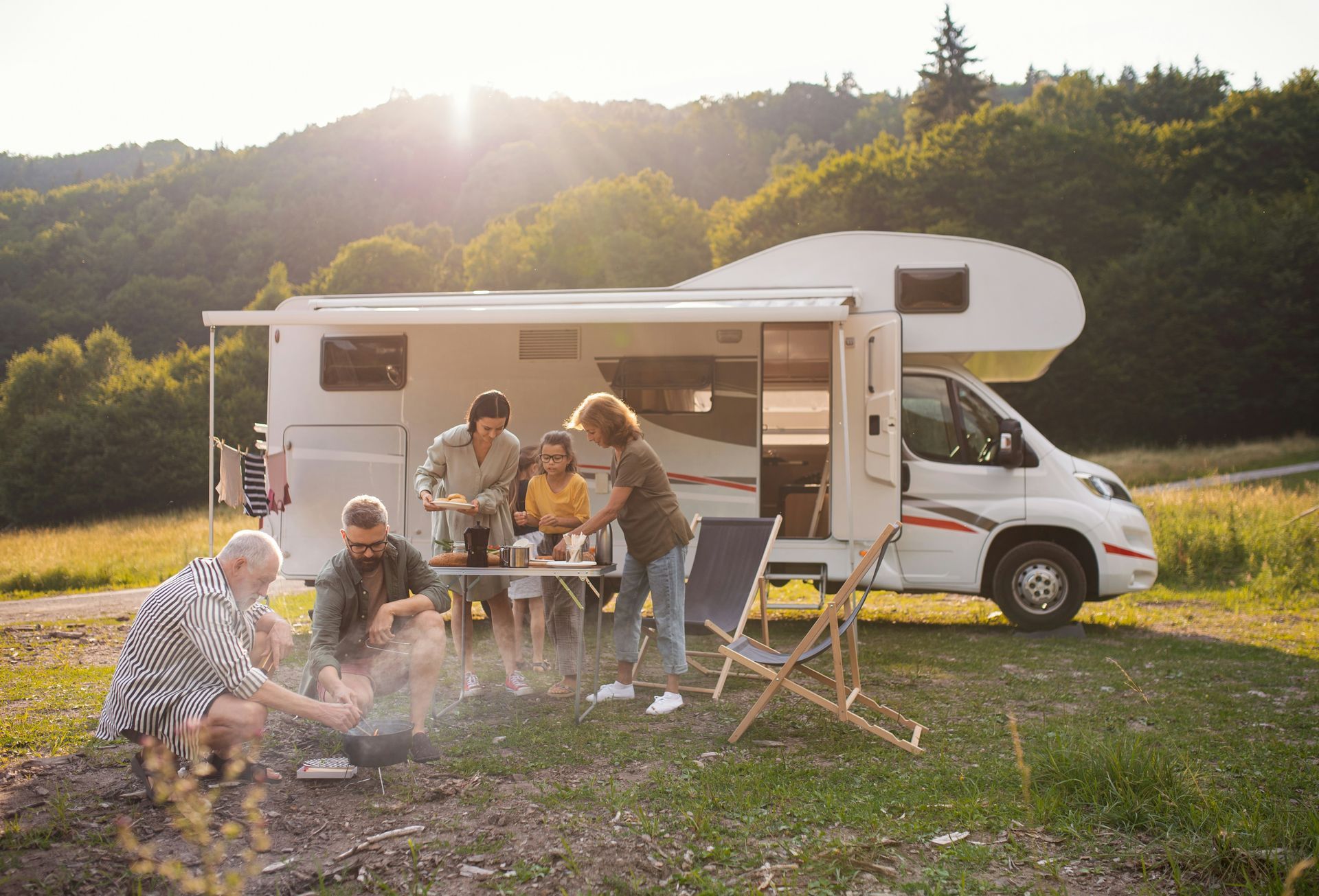 A group of people are sitting around a campfire in front of a rv.