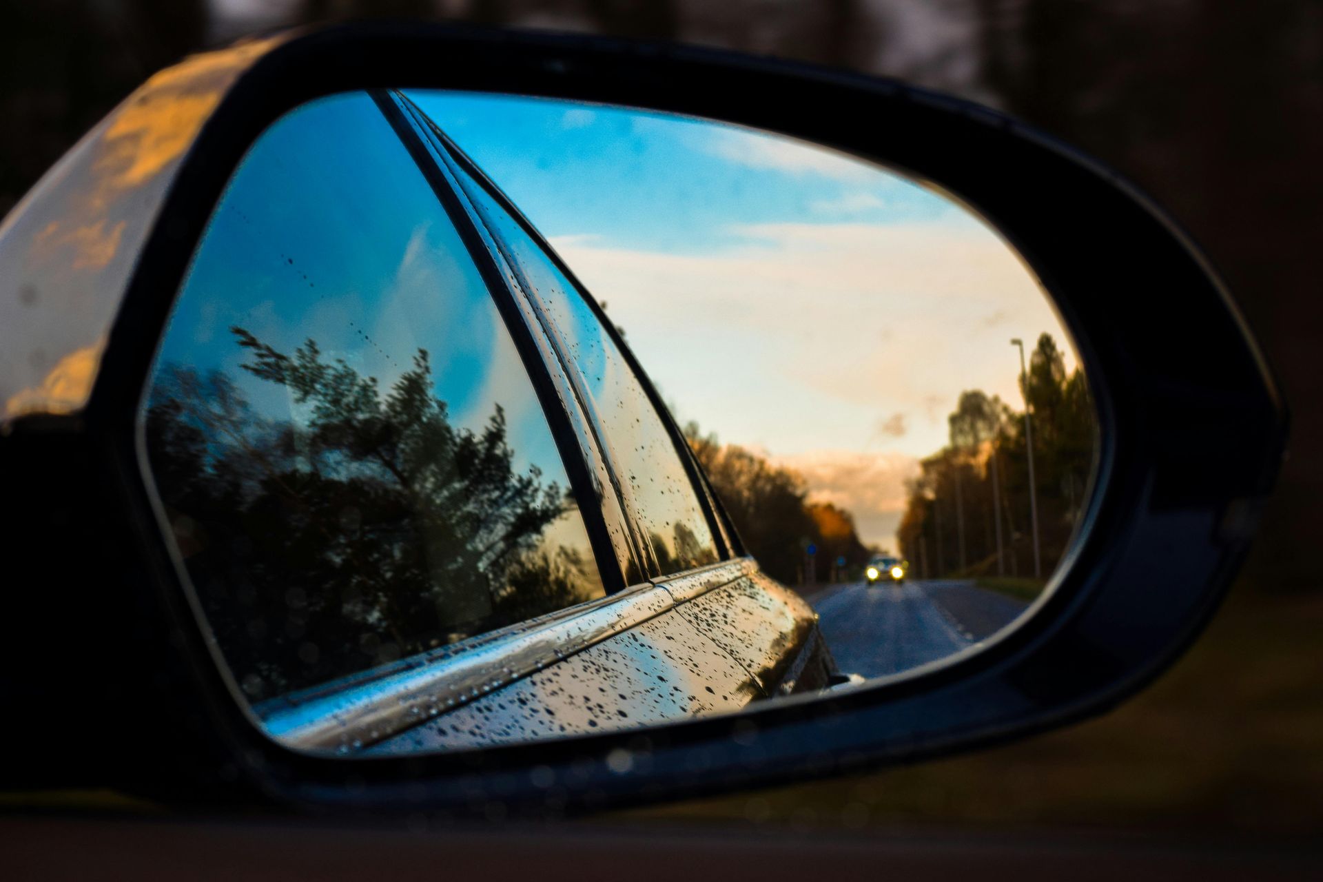 A car is driving down a road in the rear view mirror.