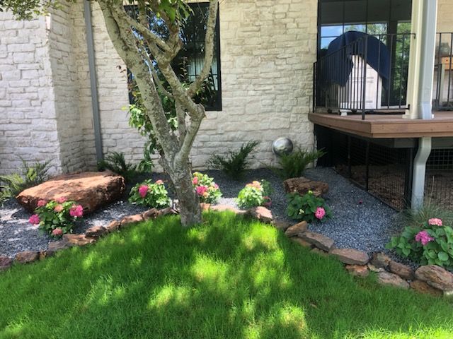 A yard with a tree and flowers in front of a brick house.
