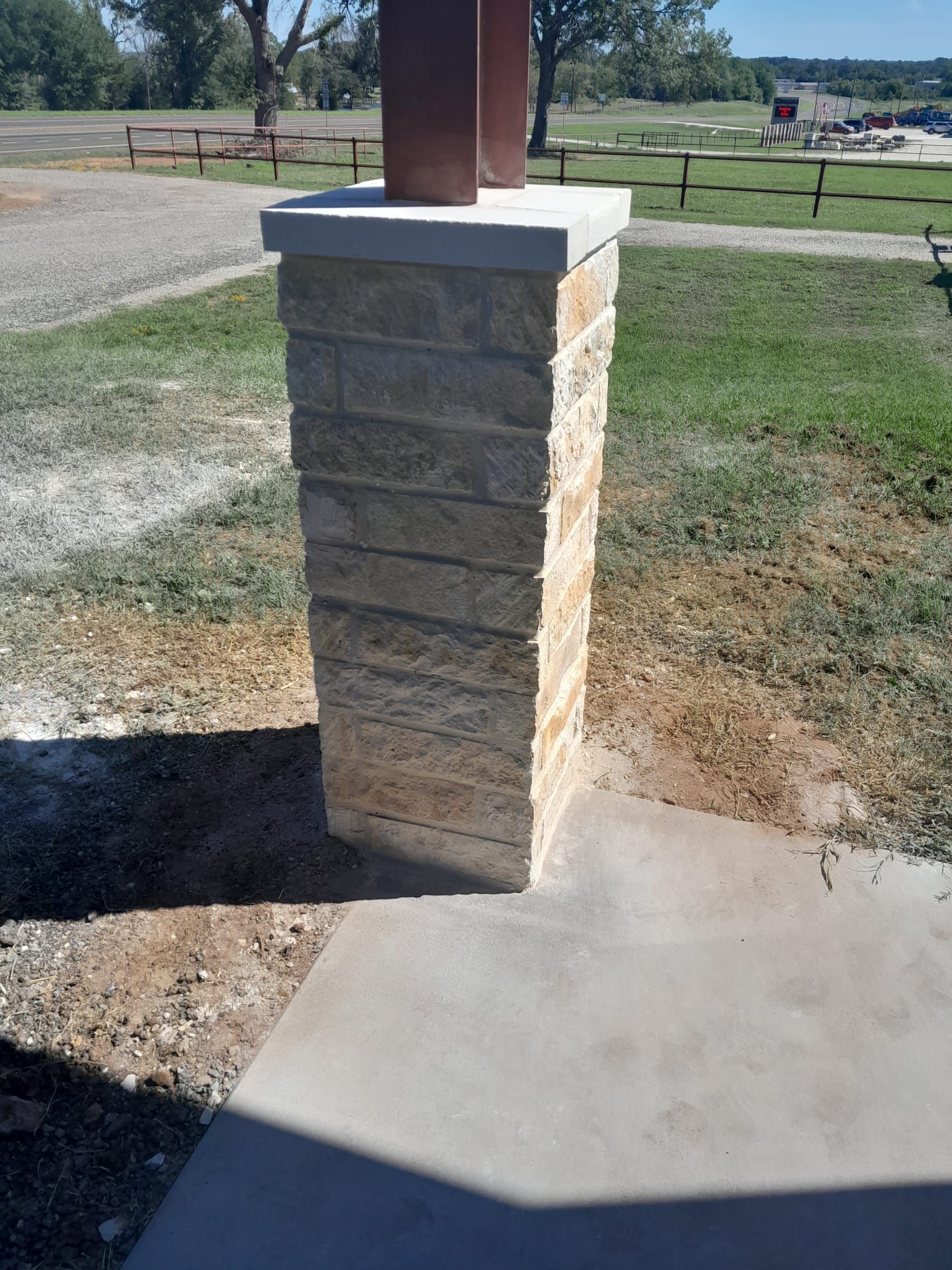 A brick column is sitting on top of a concrete walkway in a park.