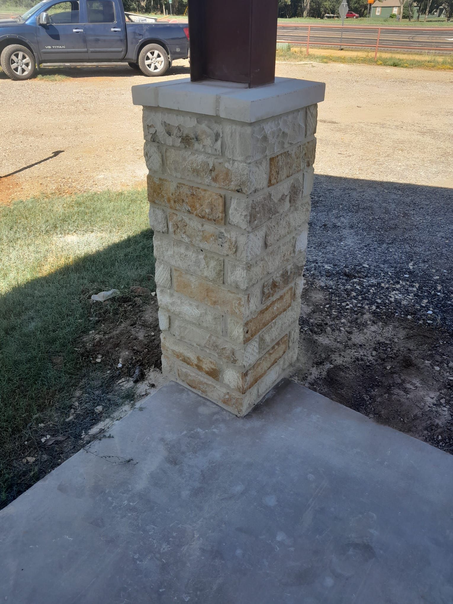 A brick column is sitting on top of a concrete patio next to a truck.