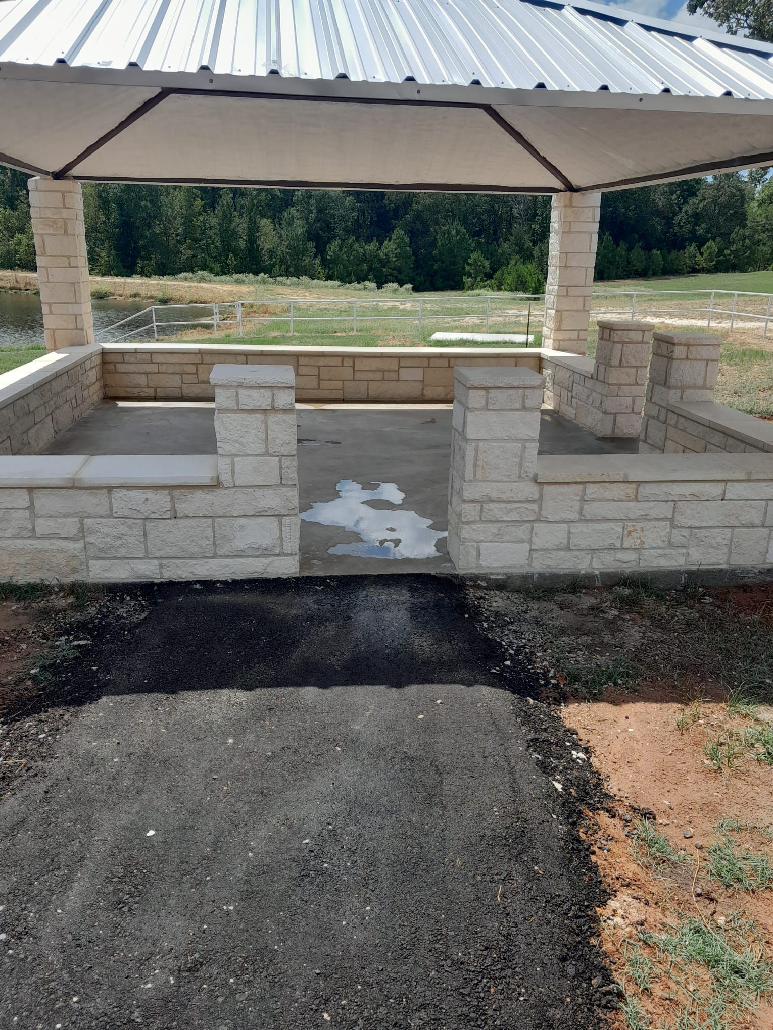 A gazebo with a brick wall and a metal roof is being built in a park.