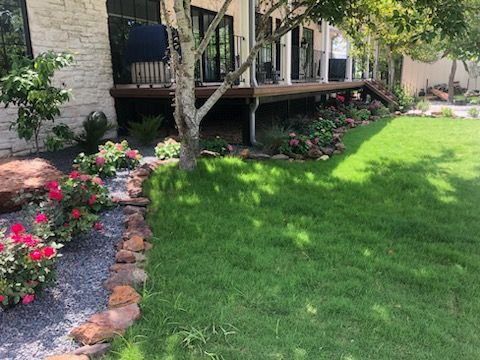 A large lawn in front of a house with a deck and flowers.