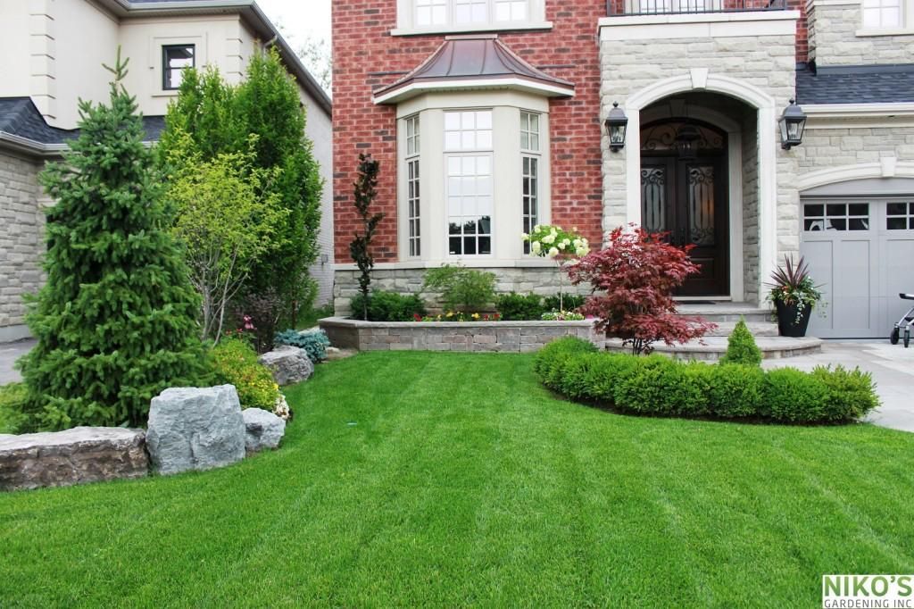 Green lawn leading to a red brick and stone house with landscaped yard.