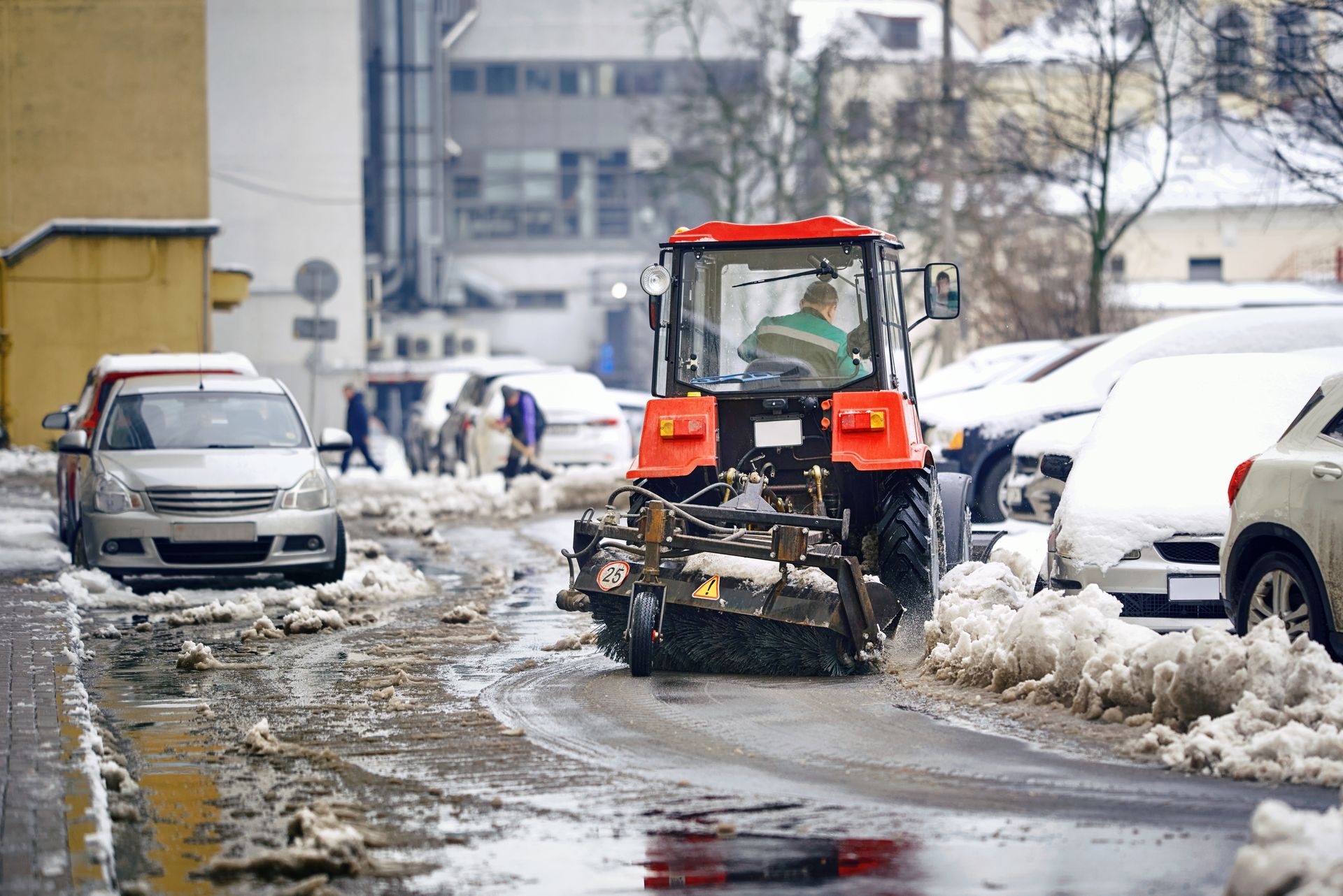 Snowplow clearing a city street with parked cars on either side.