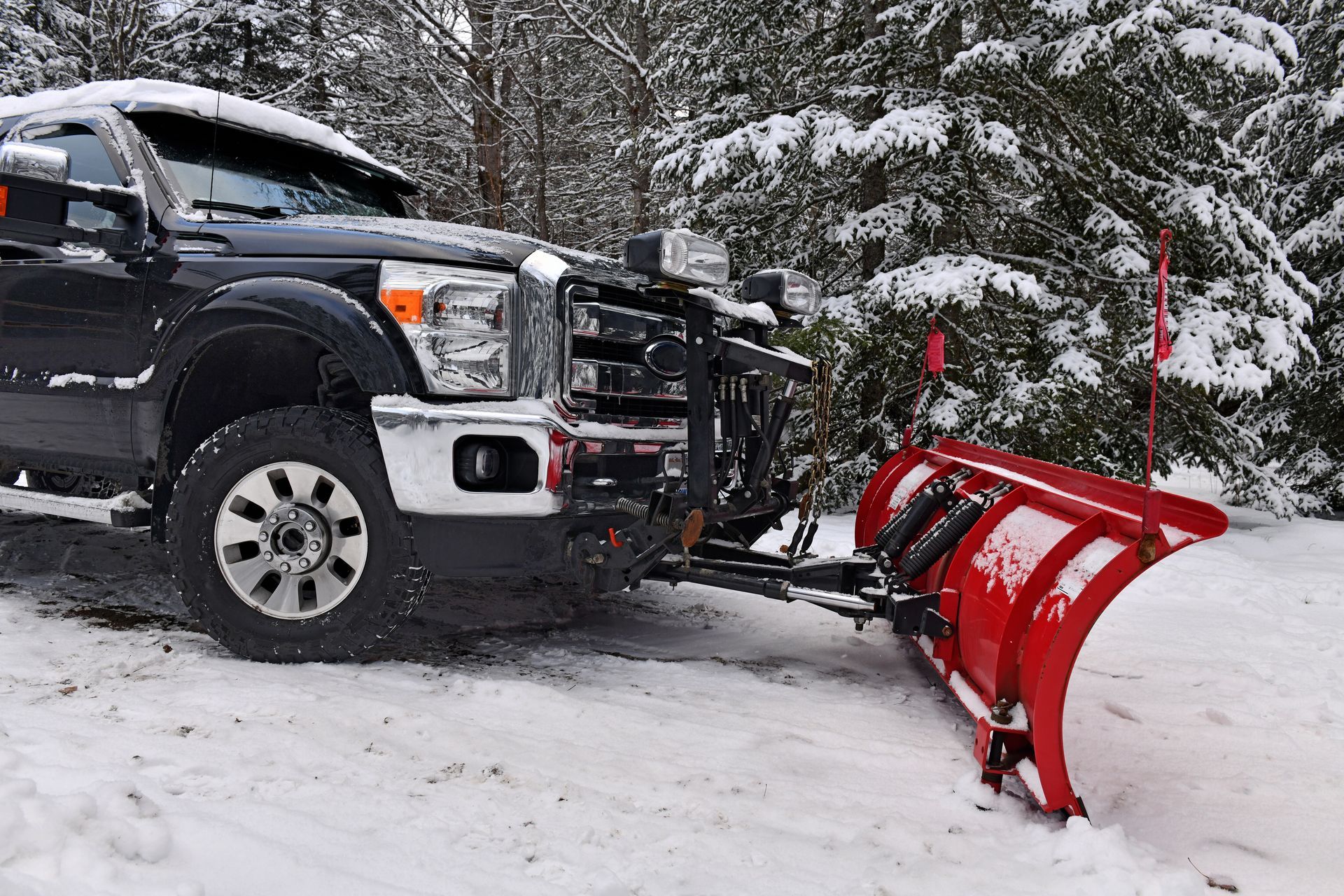 A black truck with a red snow plow attached to it is parked in the snow.